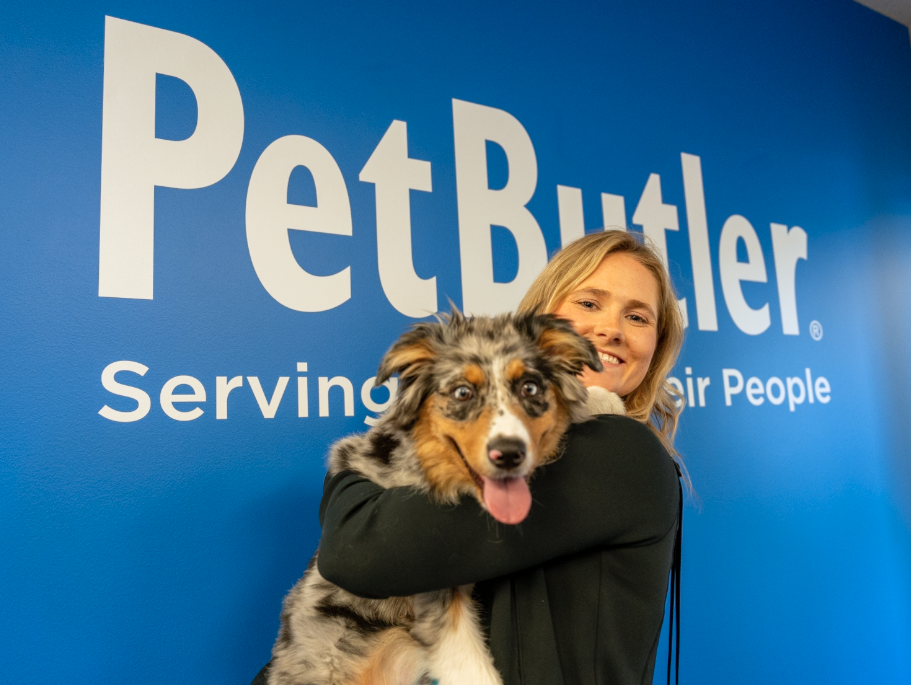 Pet Butler employee holding a dog in front of Pet Butler branded wall.